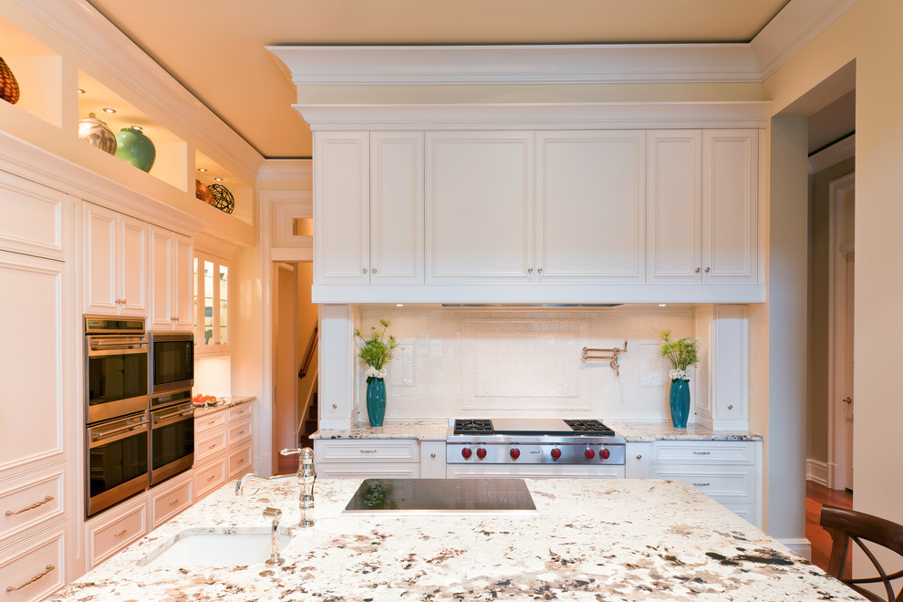 Large elegant l-shaped kitchen photo in Miami with recessed-panel cabinets, white cabinets, granite countertops, white backsplash, ceramic backsplash, paneled appliances and an island