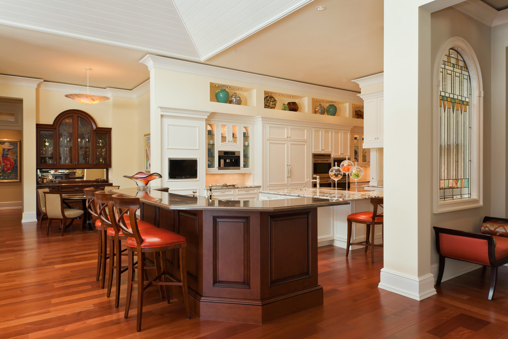 Inredning av ett klassiskt stort, avskilt l-kök, med en undermonterad diskho, luckor med infälld panel, vita skåp, granitbänkskiva, vitt stänkskydd, stänkskydd i keramik, integrerade vitvaror, mellanmörkt trägolv, en köksö och beiget golv