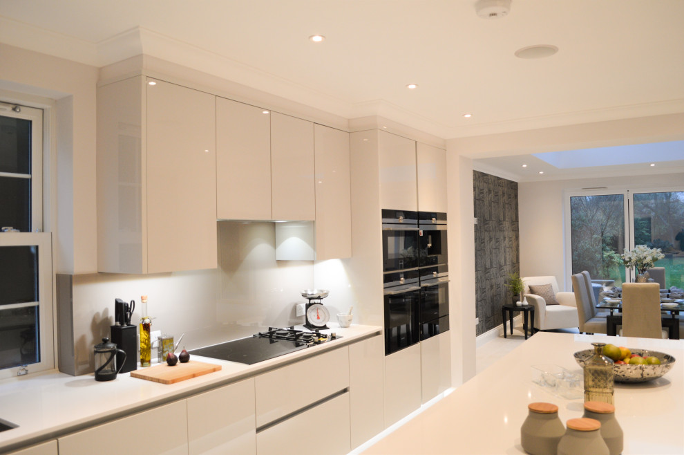 Inspiration for a large contemporary galley kitchen/diner in London with a built-in sink, flat-panel cabinets, white cabinets, white splashback, porcelain splashback, black appliances, an island and white worktops.