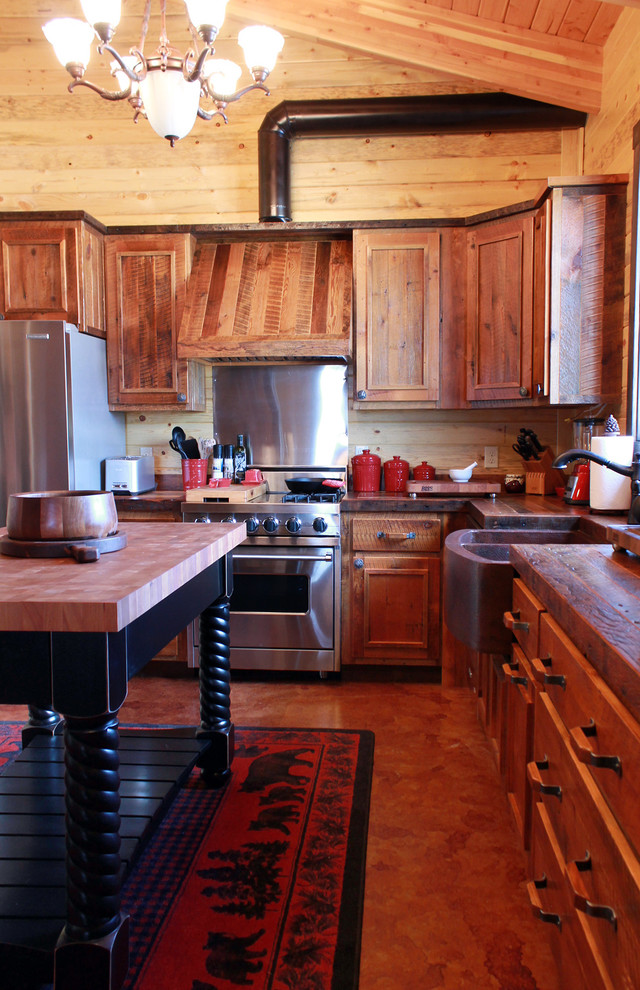 Foto på ett stort rustikt kök, med en rustik diskho, luckor med infälld panel, skåp i slitet trä, träbänkskiva, flerfärgad stänkskydd, rostfria vitvaror, betonggolv och en köksö