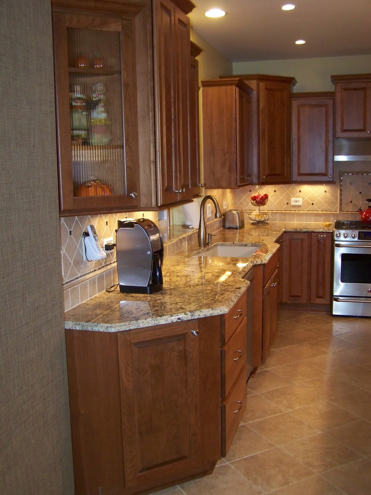 Mid-sized elegant l-shaped ceramic tile eat-in kitchen photo in Chicago with an undermount sink, raised-panel cabinets, medium tone wood cabinets, granite countertops, beige backsplash, porcelain backsplash, stainless steel appliances and an island