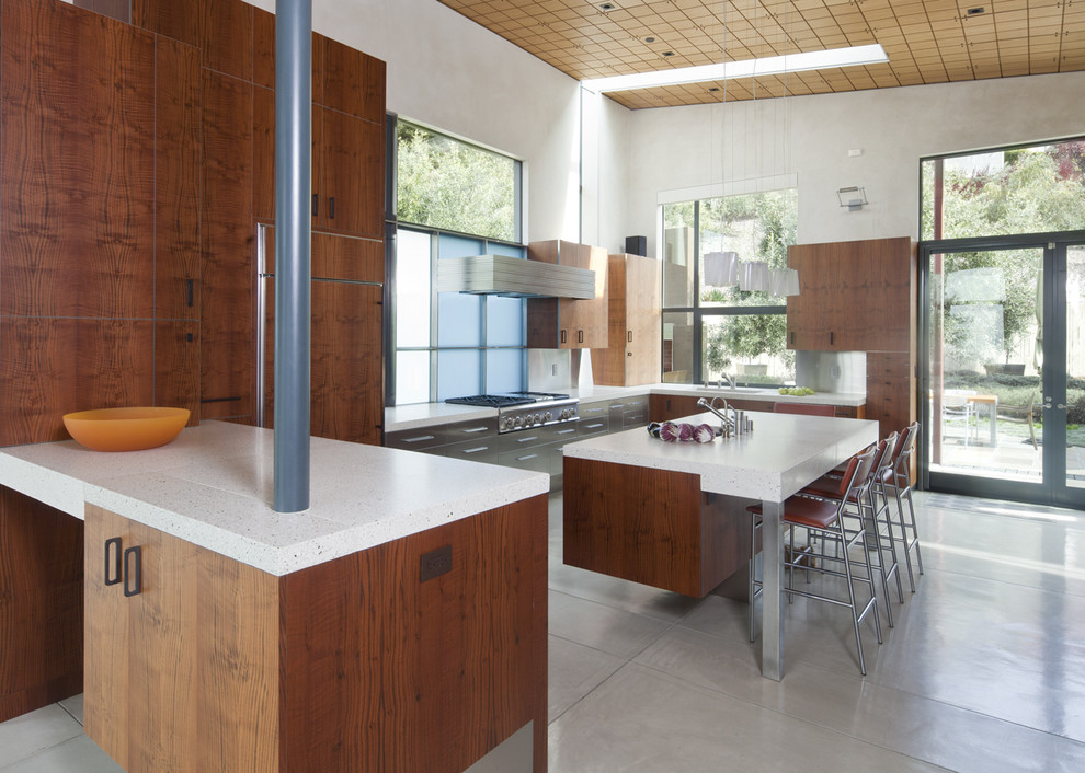 Modern inredning av ett kök, med släta luckor, skåp i mörkt trä, bänkskiva i betong, stänkskydd med metallisk yta, stänkskydd i metallkakel och integrerade vitvaror
