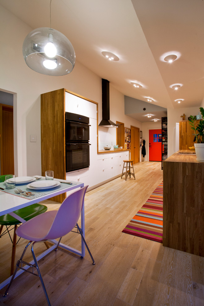 На фото: прямая кухня среднего размера в современном стиле с обеденным столом, накладной мойкой, плоскими фасадами, белыми фасадами, деревянной столешницей и светлым паркетным полом с