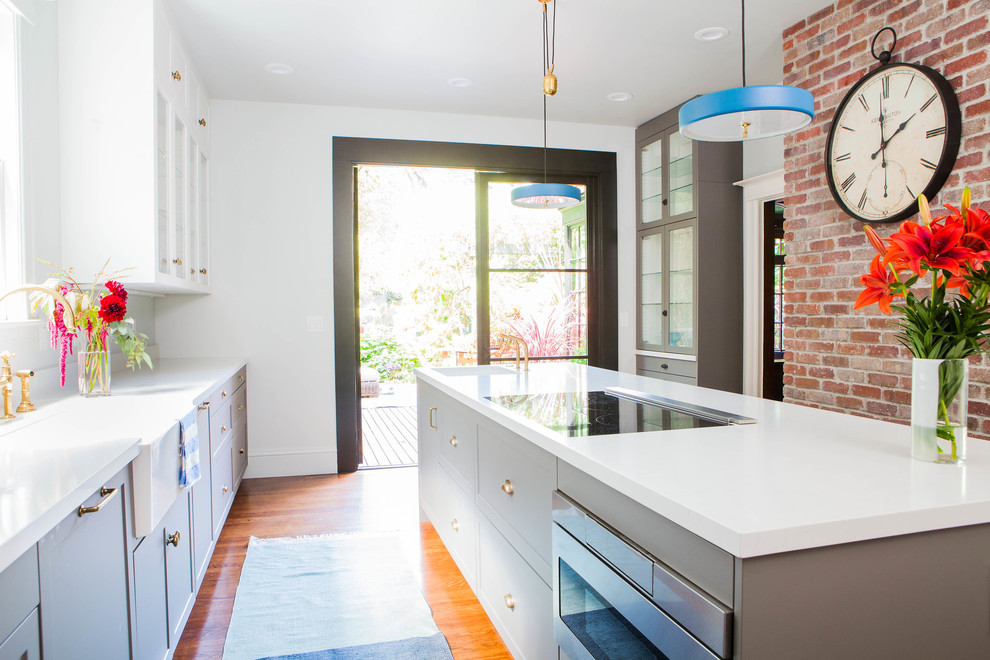 Mid-sized arts and crafts galley medium tone wood floor enclosed kitchen photo in San Francisco with shaker cabinets, gray cabinets, quartz countertops, an island, a farmhouse sink and white appliances