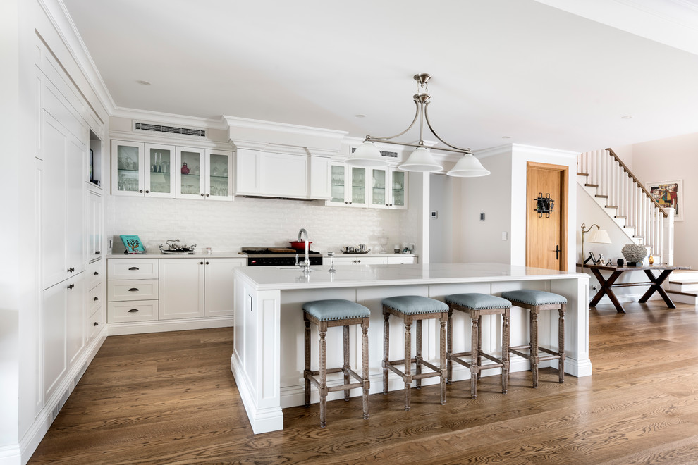 Large elegant l-shaped medium tone wood floor and brown floor kitchen photo in Perth with recessed-panel cabinets, white cabinets, quartz countertops, white backsplash, subway tile backsplash, an island, white countertops, an undermount sink and paneled appliances