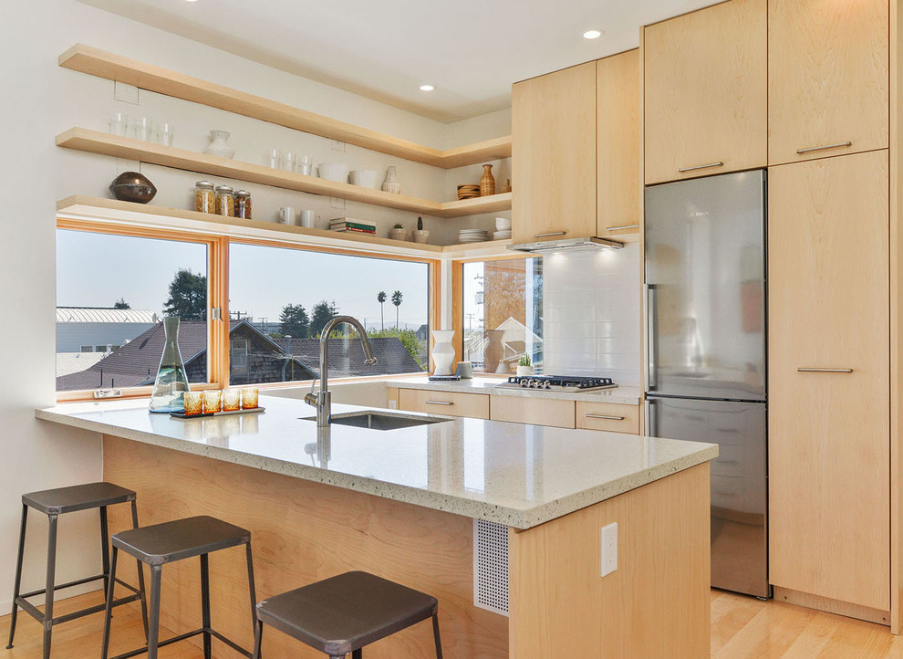 Photo of a small modern single-wall kitchen in San Francisco with flat-panel cabinets, light wood cabinets, white splashback, stainless steel appliances and a breakfast bar.
