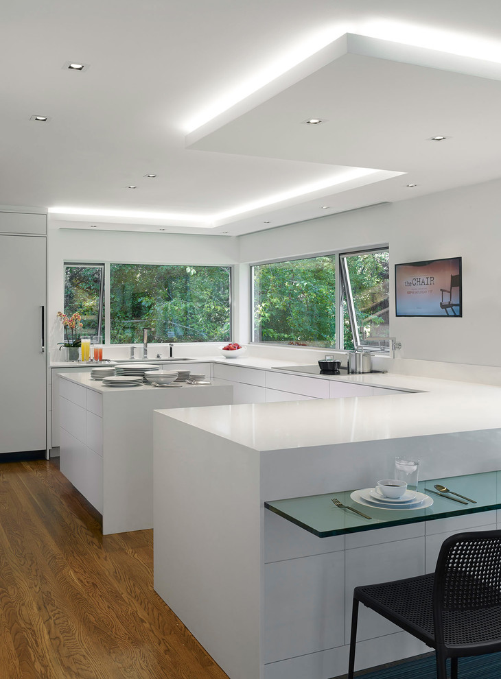 Inspiration for a large modern u-shaped kitchen/diner in San Francisco with a submerged sink, flat-panel cabinets, white cabinets, white splashback, integrated appliances, medium hardwood flooring, an island, composite countertops and brown floors.