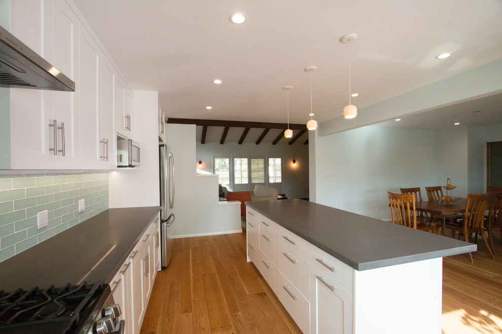 Bild på ett stort funkis kök, med en enkel diskho, skåp i shakerstil, vita skåp, bänkskiva i kvarts, grönt stänkskydd, stänkskydd i glaskakel, rostfria vitvaror, mellanmörkt trägolv, en köksö och brunt golv