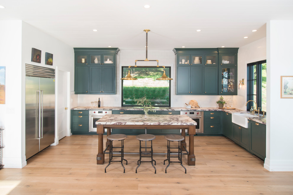 Foto på ett stort lantligt vit kök, med en nedsänkt diskho, släta luckor, gröna skåp, marmorbänkskiva, vitt stänkskydd, stänkskydd i keramik, rostfria vitvaror, mellanmörkt trägolv, en köksö och brunt golv