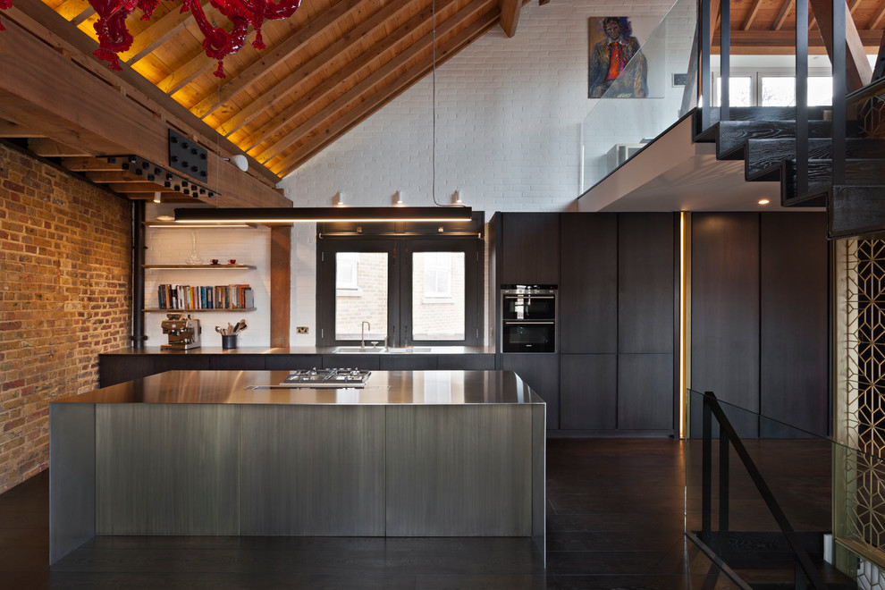 Photo of a contemporary galley open plan kitchen in London with flat-panel cabinets, black cabinets, stainless steel worktops, white splashback, brick splashback, black appliances, dark hardwood flooring, an island and brown floors.