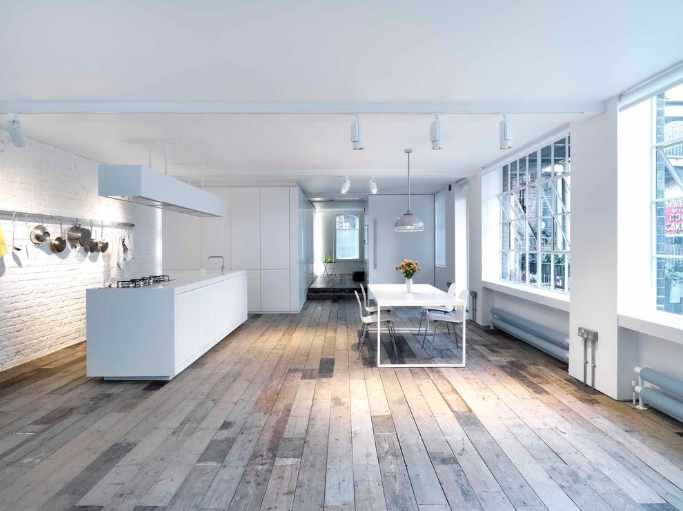 Modelo de cocina comedor urbana con armarios con paneles lisos, puertas de armario blancas, suelo de madera en tonos medios, una isla y encimera de acrílico
