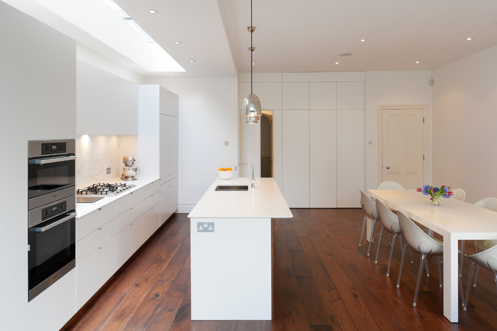 Inspiration för ett mellanstort funkis linjärt kök och matrum, med en integrerad diskho, släta luckor, vita skåp, bänkskiva i koppar, vitt stänkskydd, stänkskydd i sten, integrerade vitvaror, mellanmörkt trägolv, en köksö och brunt golv
