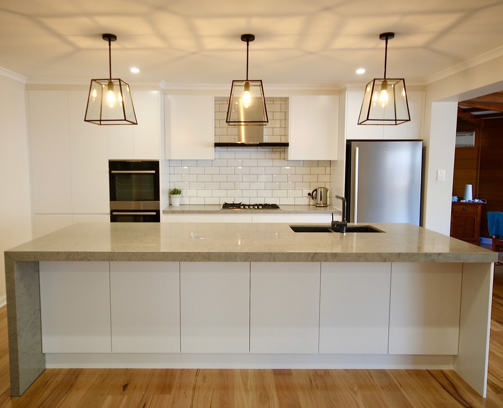 Exempel på ett mellanstort modernt linjärt kök och matrum, med en undermonterad diskho, släta luckor, vita skåp, bänkskiva i kvarts, vitt stänkskydd, stänkskydd i keramik, svarta vitvaror, mellanmörkt trägolv, en köksö och brunt golv
