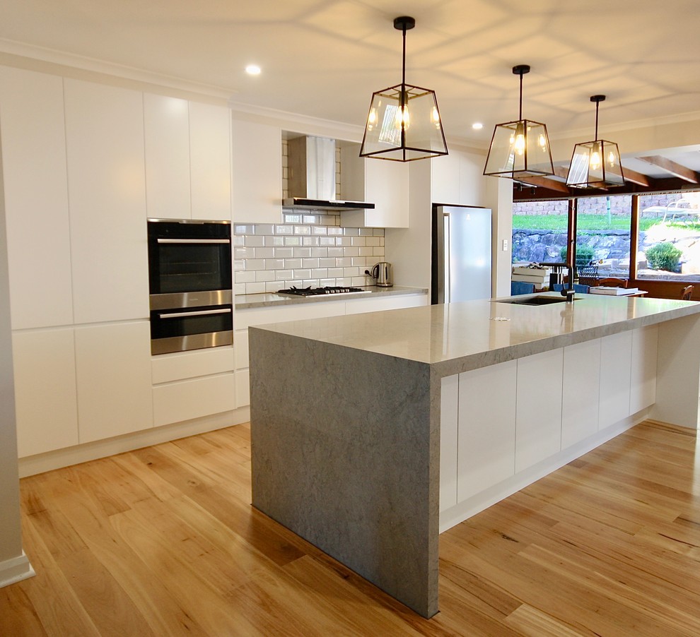 Exempel på ett mellanstort modernt linjärt kök och matrum, med en undermonterad diskho, släta luckor, vita skåp, bänkskiva i kvarts, vitt stänkskydd, stänkskydd i keramik, svarta vitvaror, mellanmörkt trägolv, en köksö och brunt golv