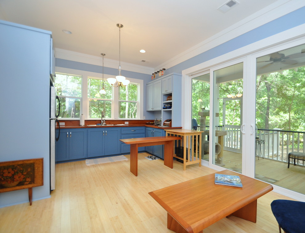 Bild på ett litet kök, med en nedsänkt diskho, släta luckor, blå skåp, träbänkskiva, rostfria vitvaror och bambugolv