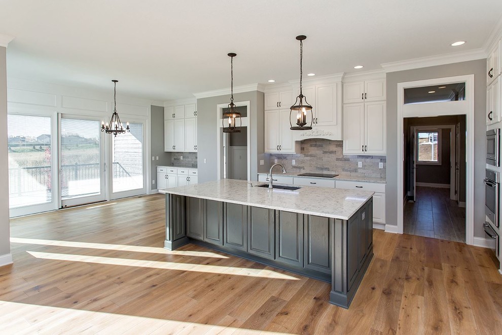 Example of a large trendy galley medium tone wood floor and beige floor open concept kitchen design in Other with raised-panel cabinets, white cabinets, an island, a single-bowl sink, marble countertops, beige backsplash, stone tile backsplash and stainless steel appliances