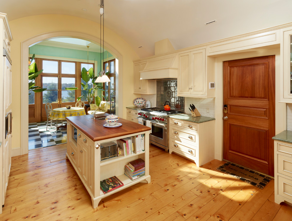 Example of a mid-sized ornate galley light wood floor and brown floor eat-in kitchen design in Boston with a drop-in sink, recessed-panel cabinets, beige cabinets, granite countertops, white backsplash, subway tile backsplash, stainless steel appliances and an island