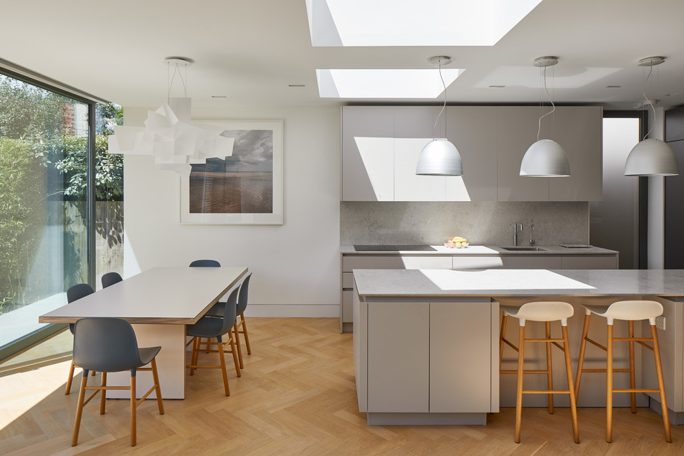 Photo of a scandi galley kitchen/diner in London with a submerged sink, flat-panel cabinets, grey cabinets, grey splashback, black appliances, light hardwood flooring, an island, beige floors and grey worktops.