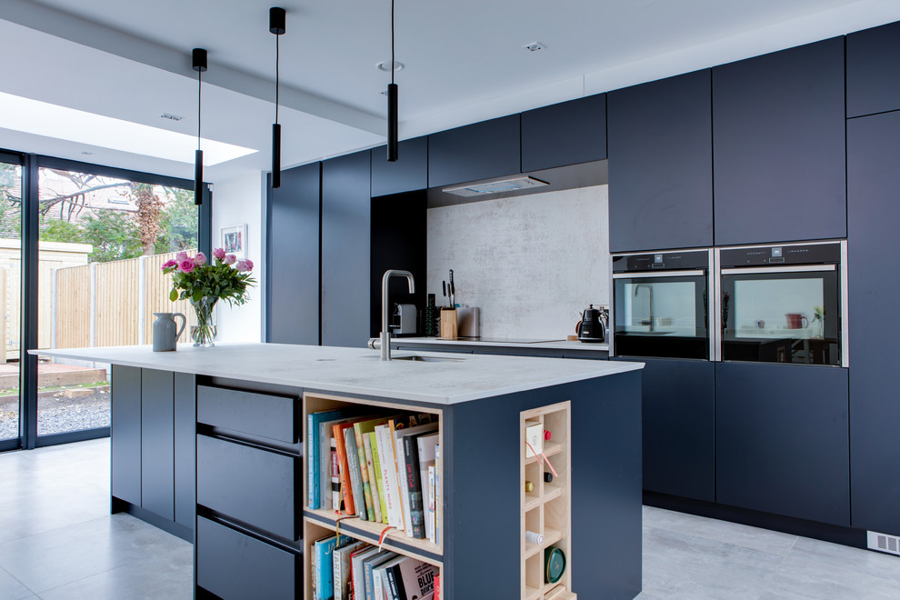 This is an example of a contemporary galley kitchen in Dublin with a submerged sink, flat-panel cabinets, blue cabinets, white splashback, stainless steel appliances, an island, grey floors and white worktops.