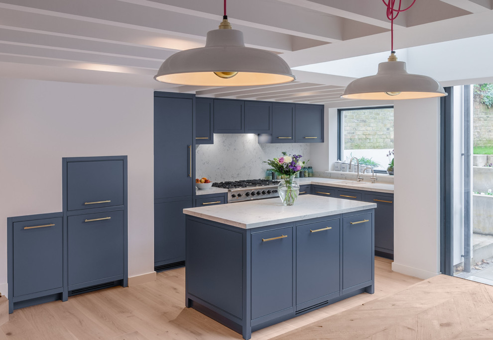 This is an example of a medium sized contemporary l-shaped kitchen/diner in London with a built-in sink, beaded cabinets, grey cabinets, composite countertops, stainless steel appliances, light hardwood flooring, an island and beige floors.