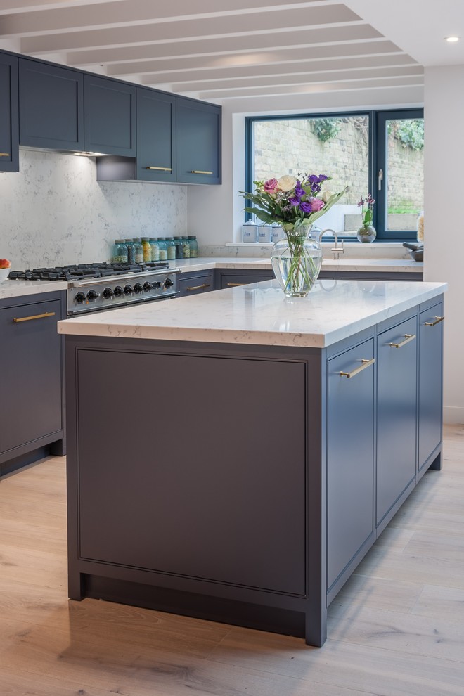This is an example of a medium sized contemporary l-shaped kitchen/diner in London with beaded cabinets, grey cabinets, composite countertops, stainless steel appliances, light hardwood flooring, an island, beige floors and a built-in sink.