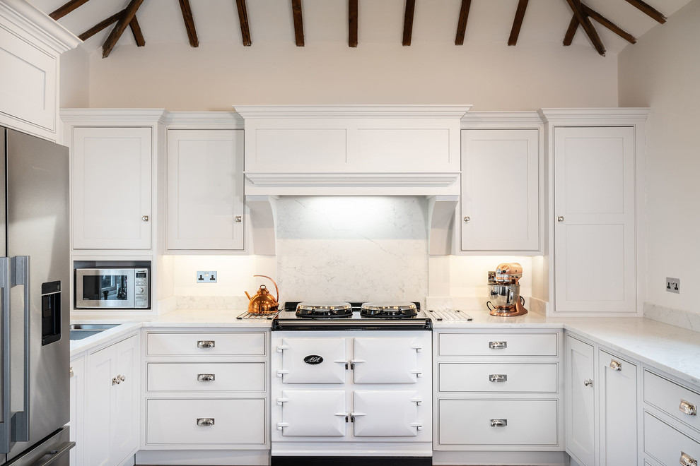 This is an example of a traditional u-shaped kitchen in Essex with white cabinets, white splashback, white worktops, beaded cabinets, stone slab splashback and white appliances.