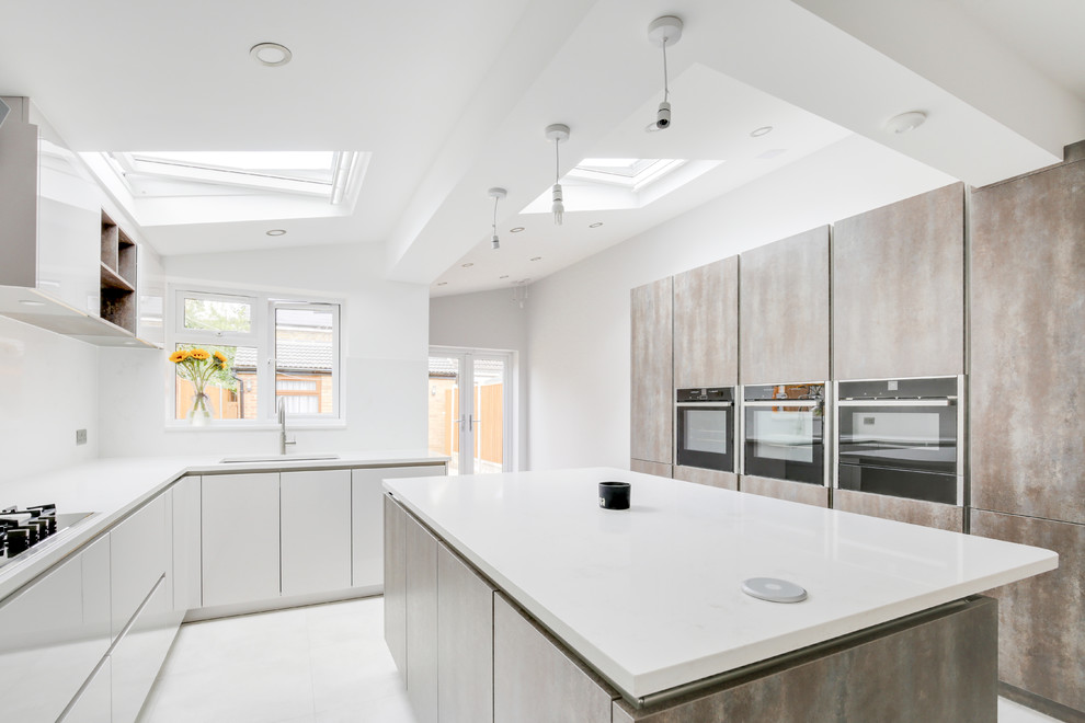 This is an example of a large modern l-shaped kitchen/diner in London with a built-in sink, flat-panel cabinets, white cabinets, quartz worktops, white splashback, stone slab splashback, stainless steel appliances, porcelain flooring, an island, white floors and white worktops.