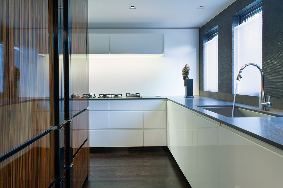 Стильный дизайн: отдельная, п-образная кухня в стиле модернизм с одинарной мойкой, плоскими фасадами, белыми фасадами и белым фартуком - последний тренд
