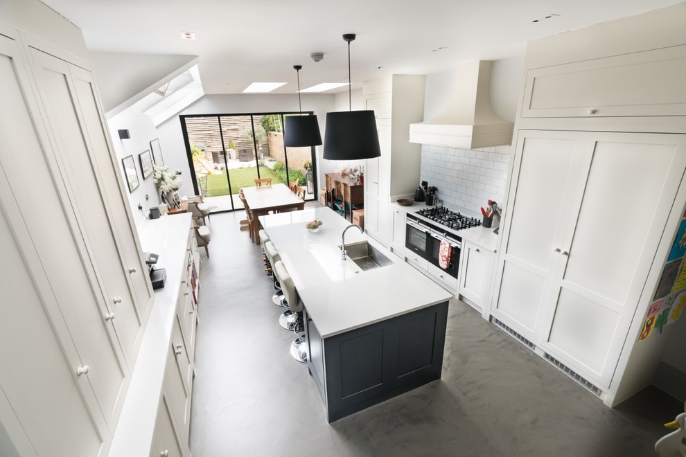 Photo of a large traditional galley open plan kitchen in London with a built-in sink, shaker cabinets, grey cabinets, composite countertops, stainless steel appliances, concrete flooring, an island, grey floors and white worktops.