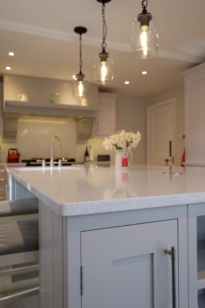 Large contemporary galley enclosed kitchen in Hampshire with a belfast sink, shaker cabinets, grey cabinets, quartz worktops, white splashback, stainless steel appliances, limestone flooring, an island, multi-coloured floors and white worktops.