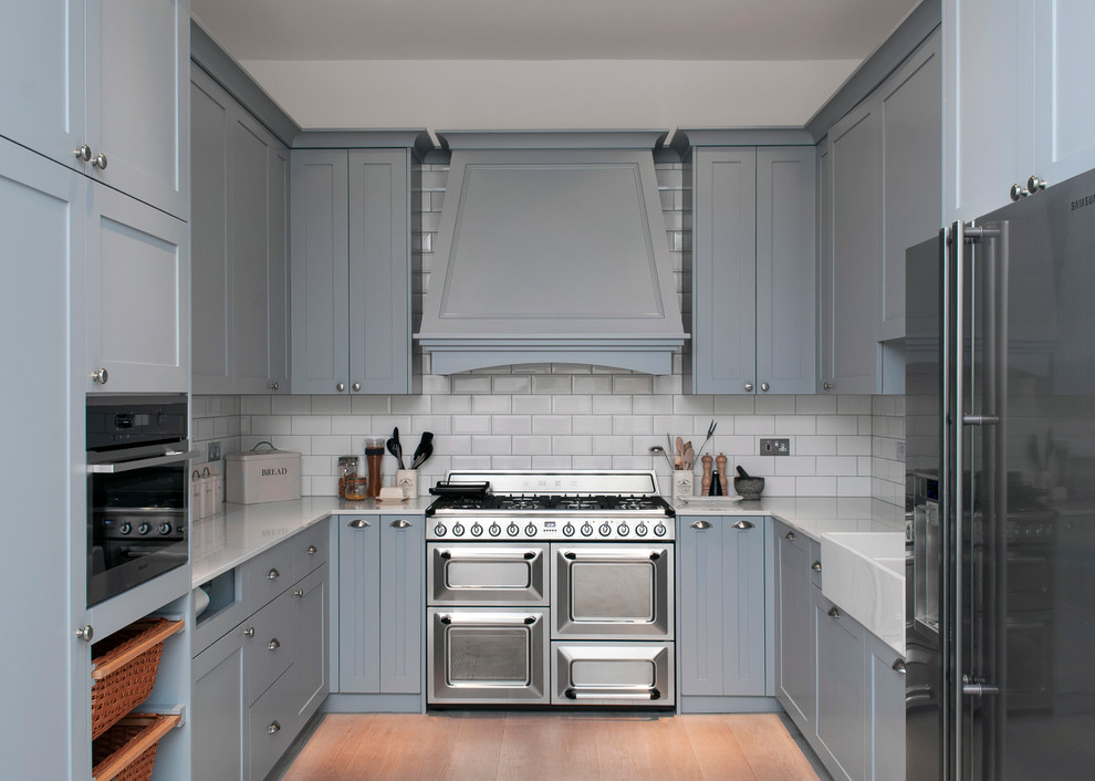 Design ideas for a small country u-shaped enclosed kitchen in London with a belfast sink, recessed-panel cabinets, blue cabinets, quartz worktops, white splashback, metro tiled splashback, stainless steel appliances, laminate floors, no island and beige floors.