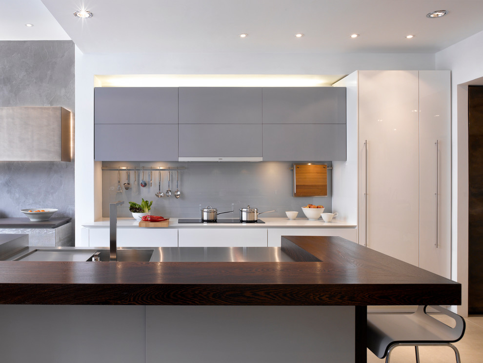 Large contemporary kitchen in London with flat-panel cabinets, grey cabinets, grey splashback, an island, wood worktops, stainless steel appliances, glass sheet splashback and a submerged sink.