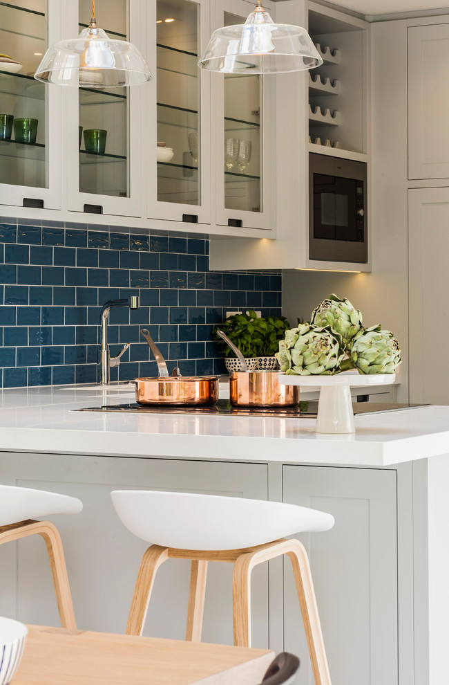 Inspiration for a mid-sized contemporary u-shaped porcelain tile and white floor eat-in kitchen remodel in London with a farmhouse sink, recessed-panel cabinets, blue cabinets, solid surface countertops, blue backsplash, ceramic backsplash, an island and white countertops