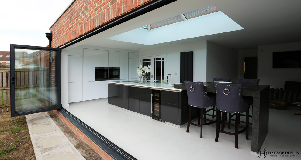Medium sized modern single-wall open plan kitchen in Other with a submerged sink, flat-panel cabinets, white cabinets, composite countertops, black appliances, ceramic flooring, an island, white floors and white worktops.