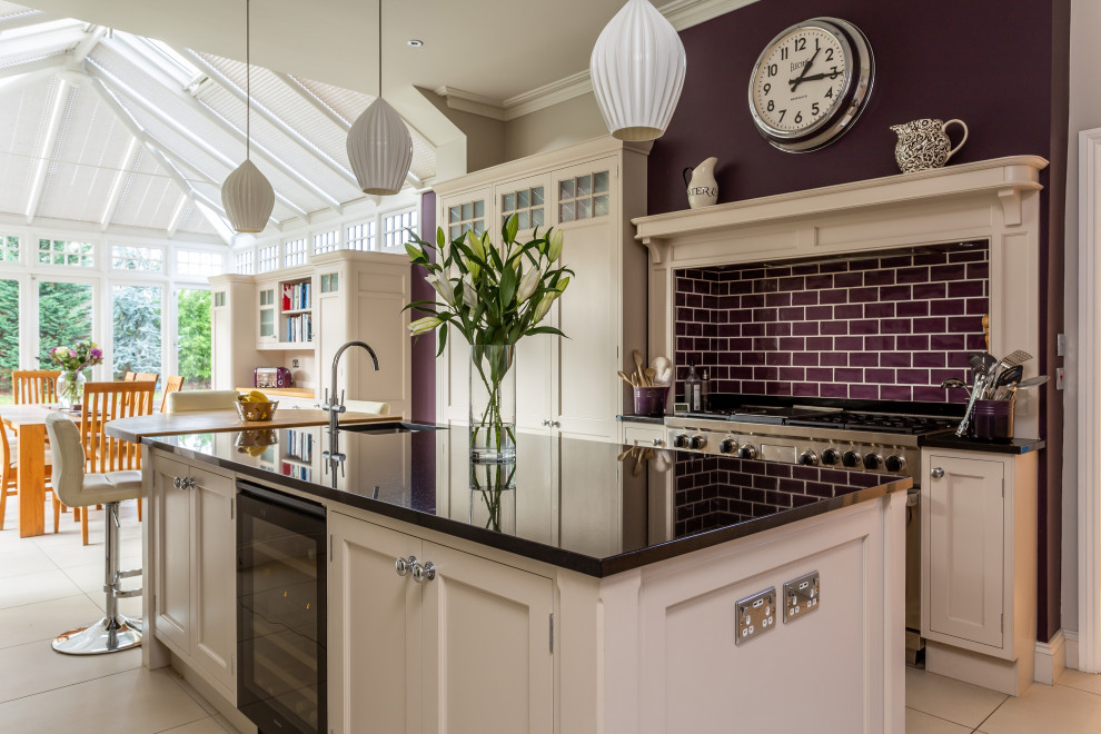 This is an example of a traditional u-shaped kitchen/diner in Hertfordshire with a submerged sink, recessed-panel cabinets, white cabinets, stainless steel appliances, an island, beige floors and black worktops.
