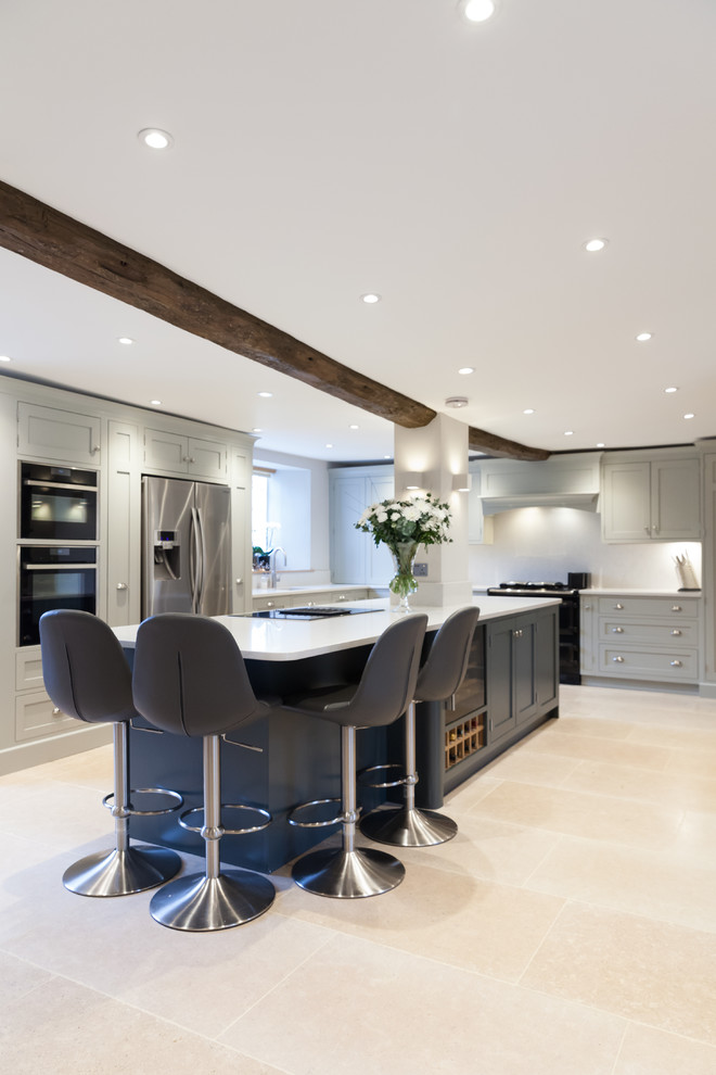 Design ideas for a large traditional l-shaped open plan kitchen in Other with a belfast sink, shaker cabinets, grey cabinets, composite countertops, white splashback, stainless steel appliances, limestone flooring, an island and beige floors.