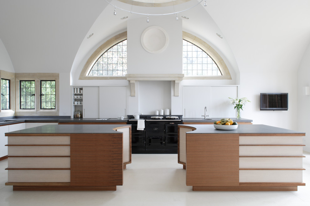 Aménagement d'une grande cuisine ouverte moderne en L et bois brun avec un plan de travail en granite et 2 îlots.