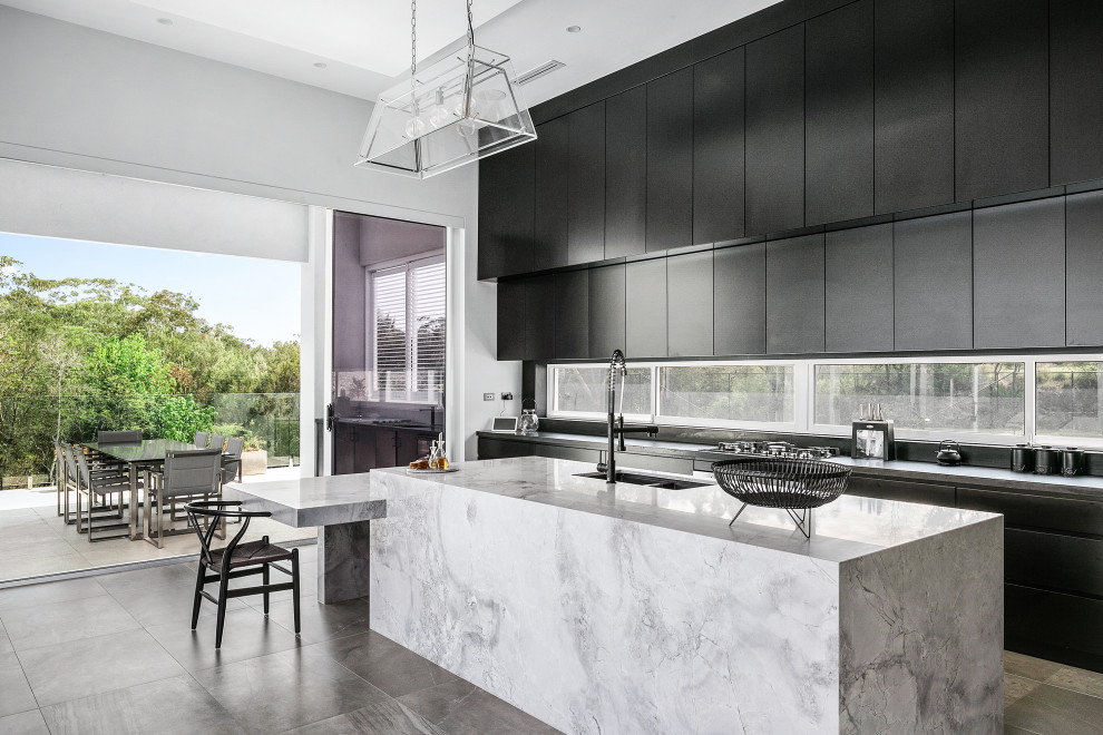 Modern inredning av ett mycket stort vit linjärt vitt kök med öppen planlösning, med en dubbel diskho, släta luckor, svarta skåp, marmorbänkskiva, fönster som stänkskydd, svarta vitvaror, en köksö och grått golv
