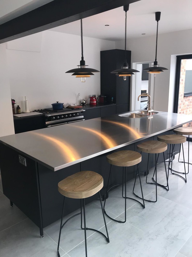 This is an example of a medium sized industrial single-wall kitchen/diner in Other with an integrated sink, flat-panel cabinets, black cabinets, stainless steel worktops, porcelain flooring, an island and grey floors.