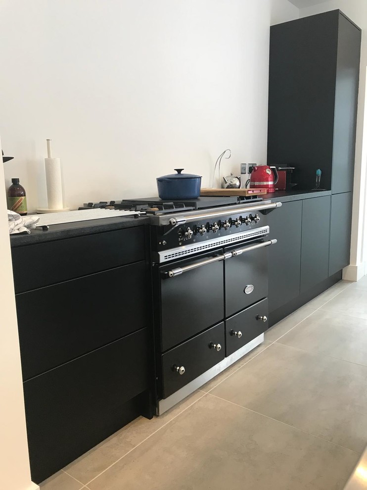 Exempel på ett mellanstort industriellt linjärt kök och matrum, med en integrerad diskho, släta luckor, svarta skåp, bänkskiva i rostfritt stål, klinkergolv i porslin, en köksö och grått golv