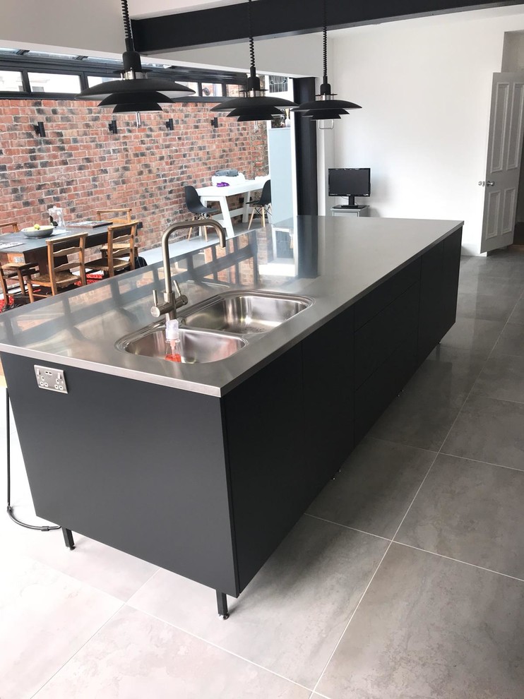 Design ideas for a medium sized urban single-wall kitchen/diner in Other with an integrated sink, flat-panel cabinets, black cabinets, stainless steel worktops, porcelain flooring, an island and grey floors.