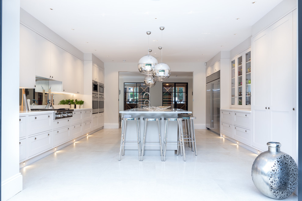 Example of a trendy u-shaped beige floor enclosed kitchen design in Berkshire with shaker cabinets, white cabinets, stainless steel appliances, an island and white countertops