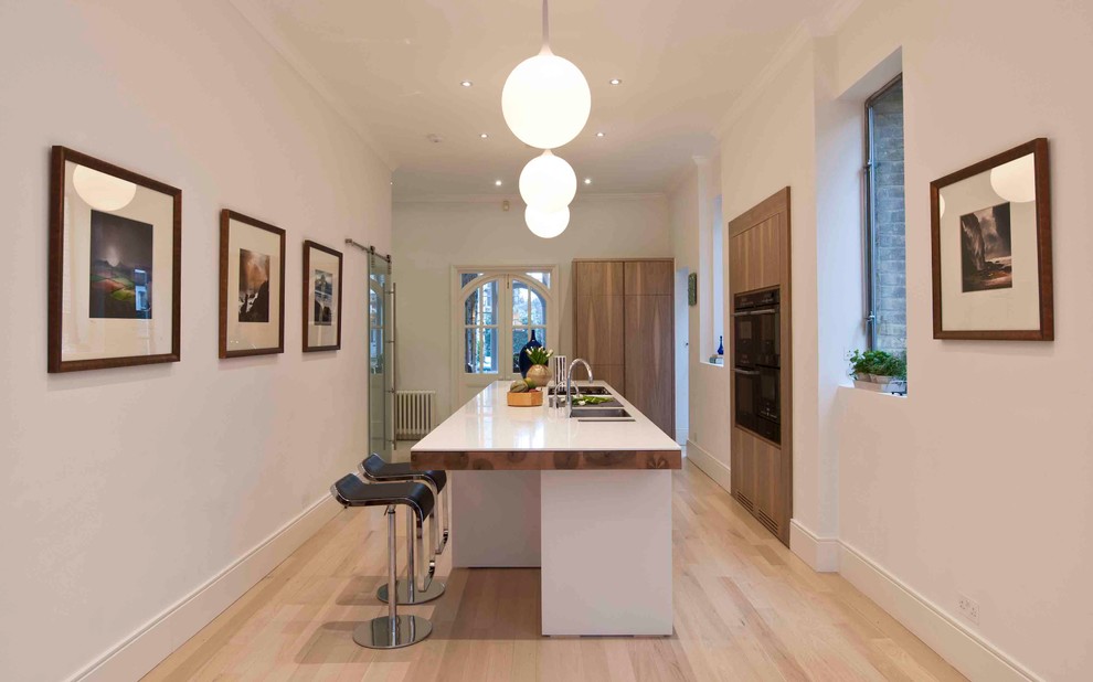 Huge trendy single-wall light wood floor eat-in kitchen photo in London with an undermount sink, flat-panel cabinets, medium tone wood cabinets, quartz countertops, black appliances and an island