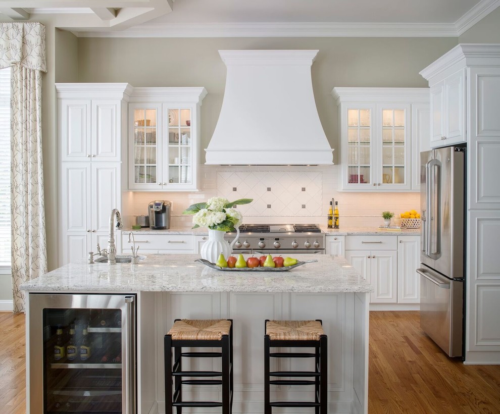 This is an example of a medium sized traditional kitchen in DC Metro with a submerged sink, white cabinets, stainless steel appliances, medium hardwood flooring, an island, glass-front cabinets and white splashback.
