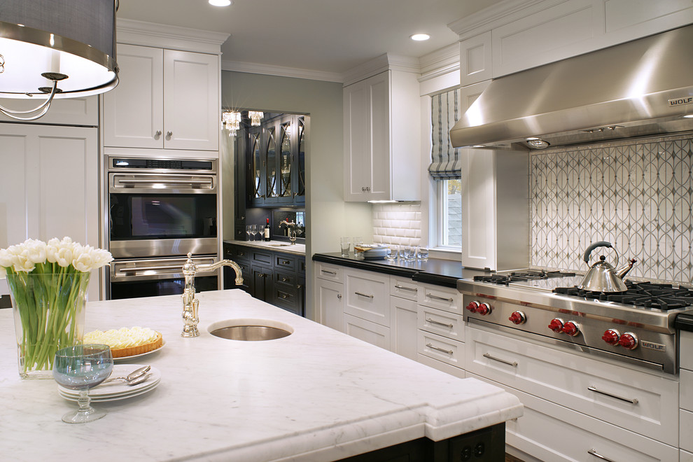 Photo of a traditional u-shaped kitchen/diner in New York with a belfast sink, recessed-panel cabinets, white cabinets, marble worktops, grey splashback and stainless steel appliances.