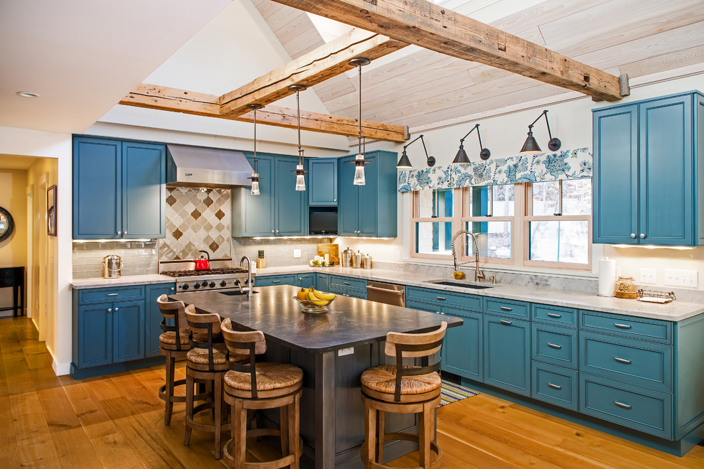Bild på ett stort maritimt kök, med en undermonterad diskho, grått stänkskydd, stänkskydd i glaskakel, rostfria vitvaror, mellanmörkt trägolv, luckor med infälld panel, blå skåp, marmorbänkskiva och en köksö
