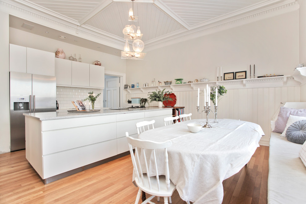 Bild på ett vintage kök och matrum, med släta luckor, vita skåp, vitt stänkskydd, stänkskydd i tunnelbanekakel och rostfria vitvaror