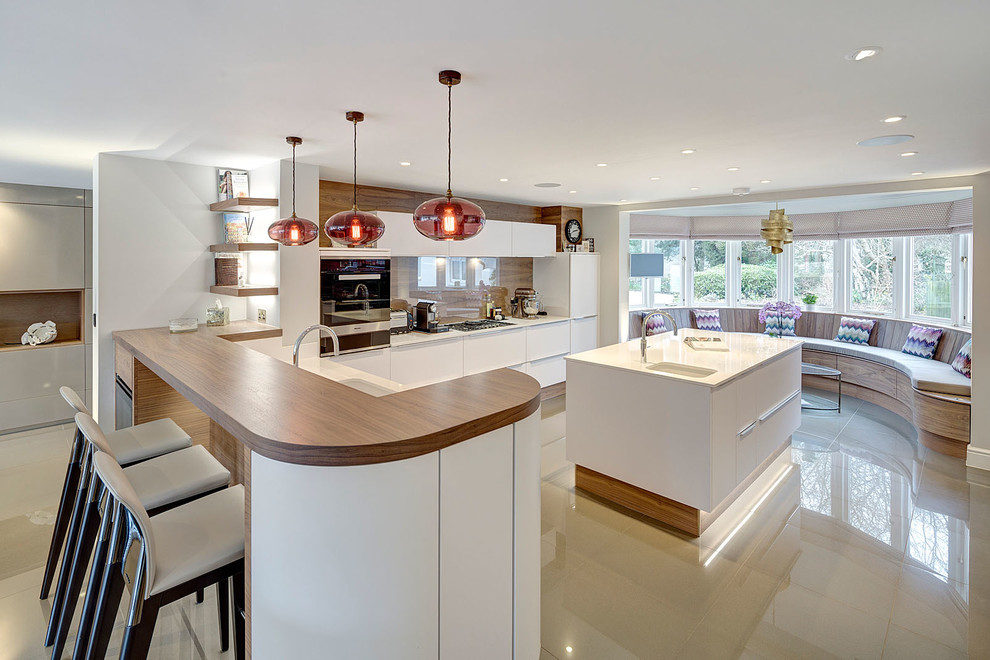 Moderne Küche in U-Form mit flächenbündigen Schrankfronten, weißen Schränken, Glasrückwand, Kücheninsel, Doppelwaschbecken und Elektrogeräten mit Frontblende in Surrey