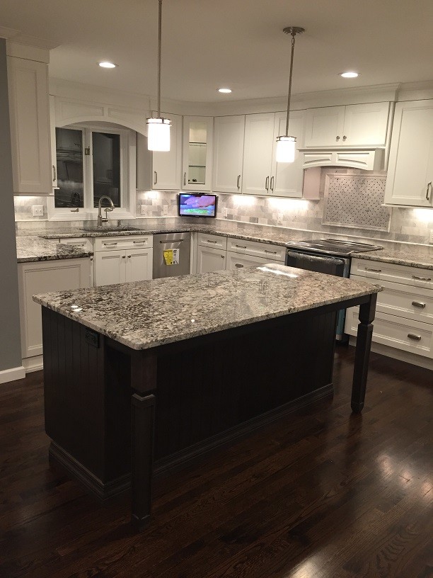 Photo of a large modern l-shaped kitchen/diner in New York with a single-bowl sink, shaker cabinets, white cabinets, granite worktops, grey splashback, stone tiled splashback, stainless steel appliances, dark hardwood flooring and an island.