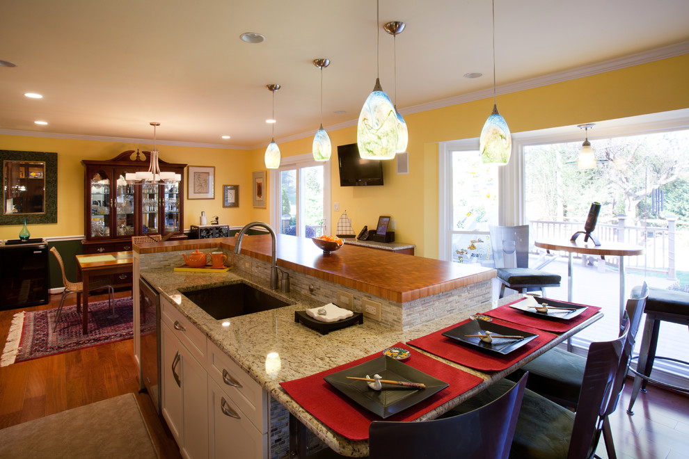 Bild på ett funkis kök och matrum, med en enkel diskho, släta luckor, skåp i mörkt trä, granitbänkskiva, flerfärgad stänkskydd, stänkskydd i stickkakel, rostfria vitvaror, mellanmörkt trägolv och en köksö